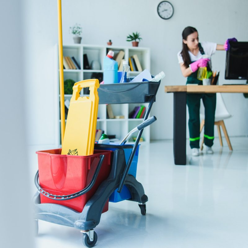 young-female-janitor-cleaning-office-with-various-cleaning-equipment.jpg